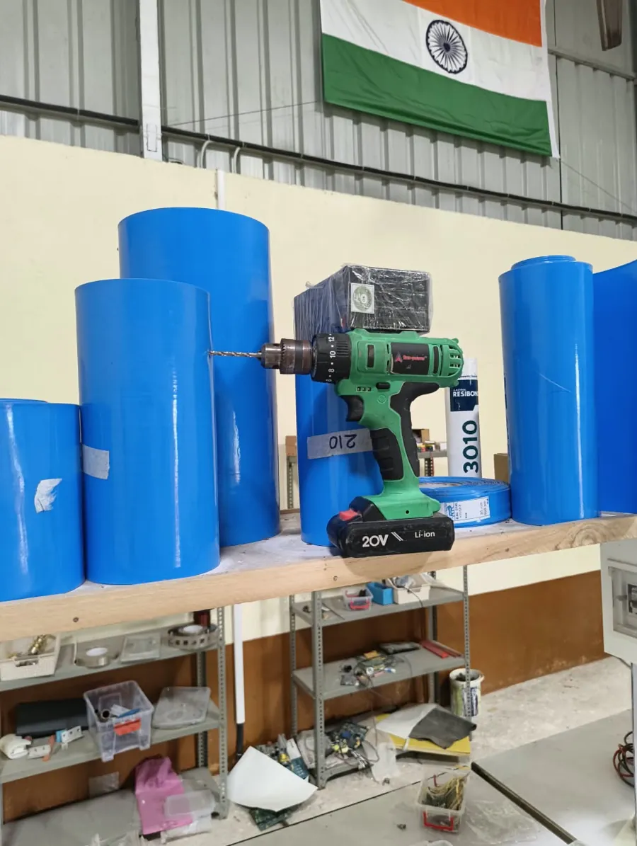 Battery pack wraps and tools in the Anant Energies assembly unit, with the Indian flag on the wall